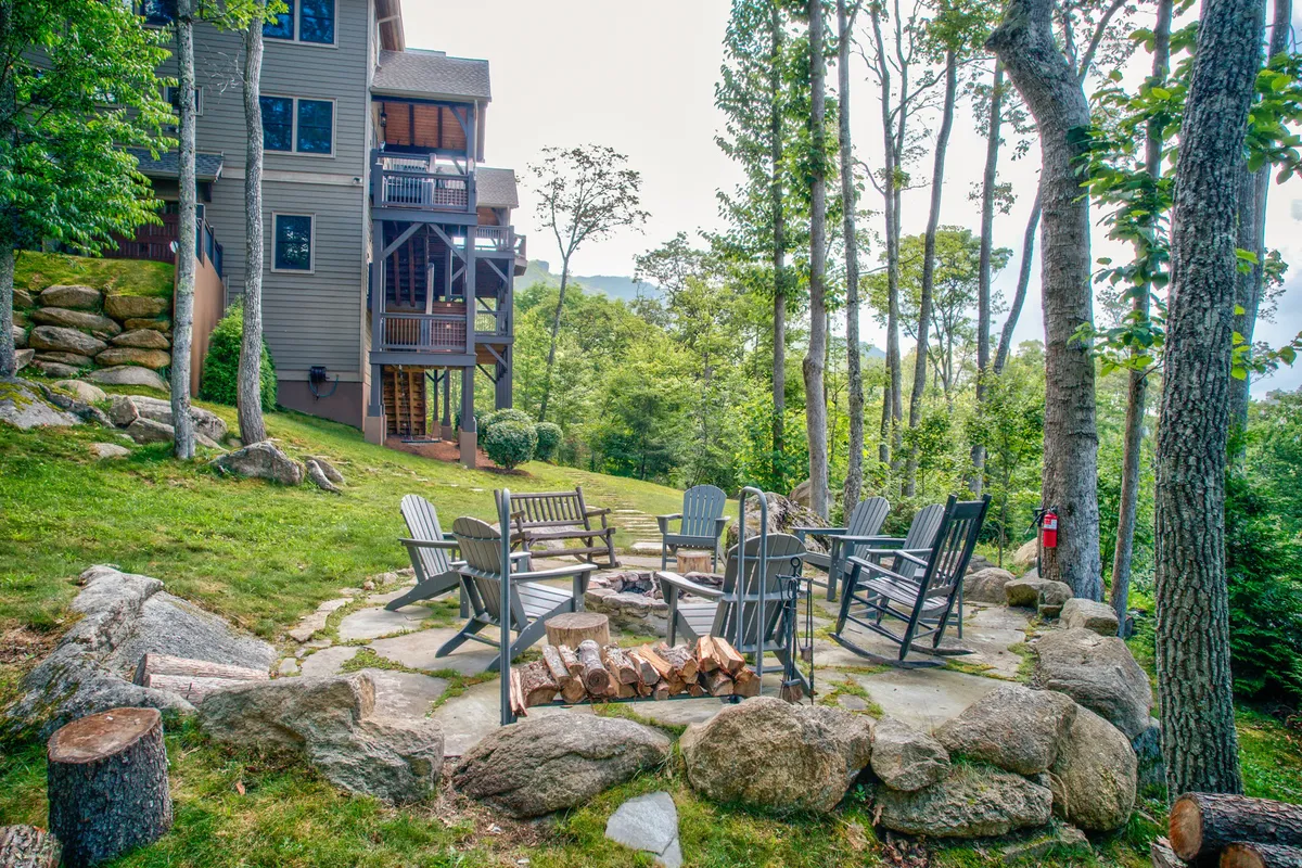 An inviting exterior fire pit area surrounded by wooden seating and lush trees, creating a perfect spot for gathering under the stars to share stories, roast s’mores, and unwind after a day of play.
