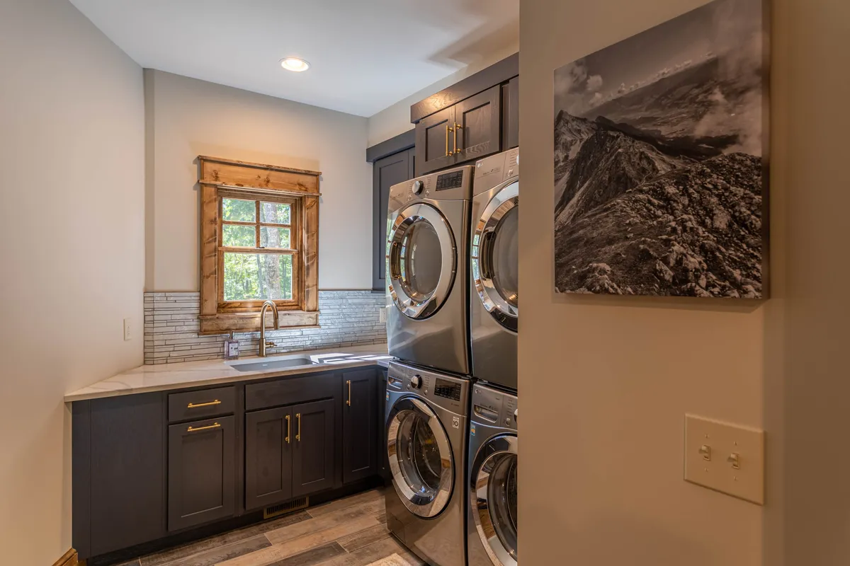 A modern laundry room with dual washer and dryer units, a sink, and natural light from a window. The space is organized and upscale, making household tasks pleasant and efficient.