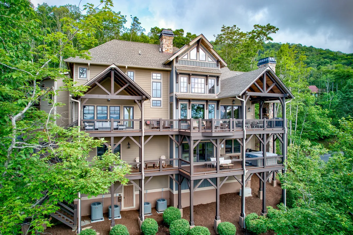 A spacious outdoor deck attached to a stately house, surrounded by lush greenery and set up for gatherings. The area is ideal for outdoor meetings, barbecues, or relaxing together after a productive day. The tranquil setting is framed by natural foliage, suggesting privacy and inspiration from the mountain environment.