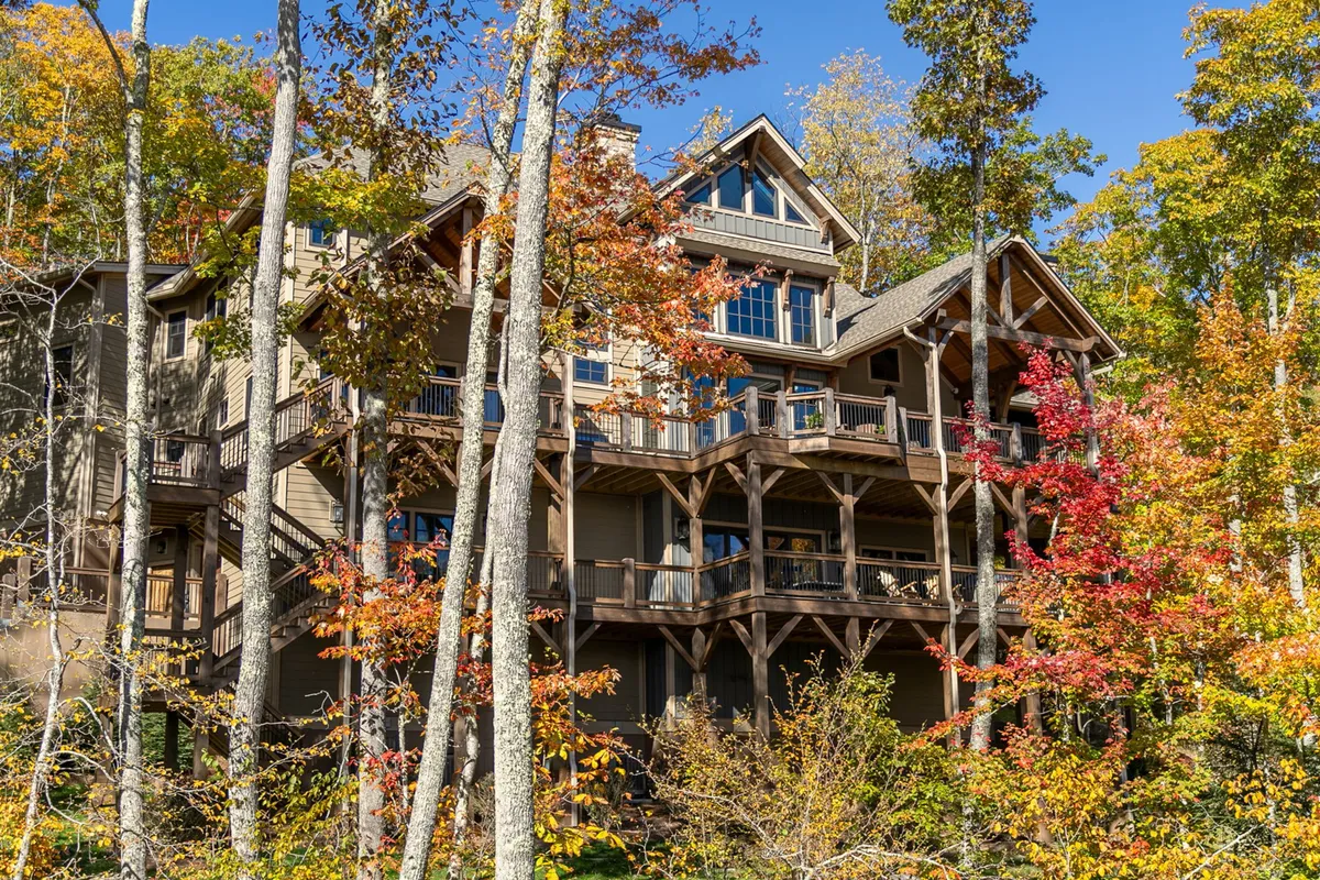 A three-story wooden house surrounded by vibrant autumn foliage and trees. The balconies and outdoor spaces are visible, hinting at areas ideal for gatherings, relaxation, and enjoying the beautiful mountain environment with loved ones.