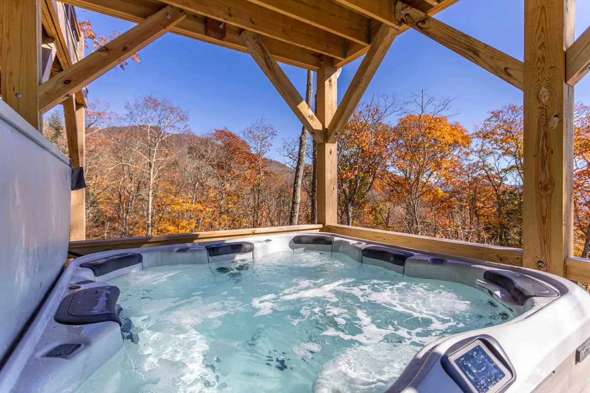 A serene exterior view featuring a hot tub nestled among trees with a breathtaking mountain view in the background. The scene conveys relaxation and immersion in natural beauty, with the hot tub as the focal point.