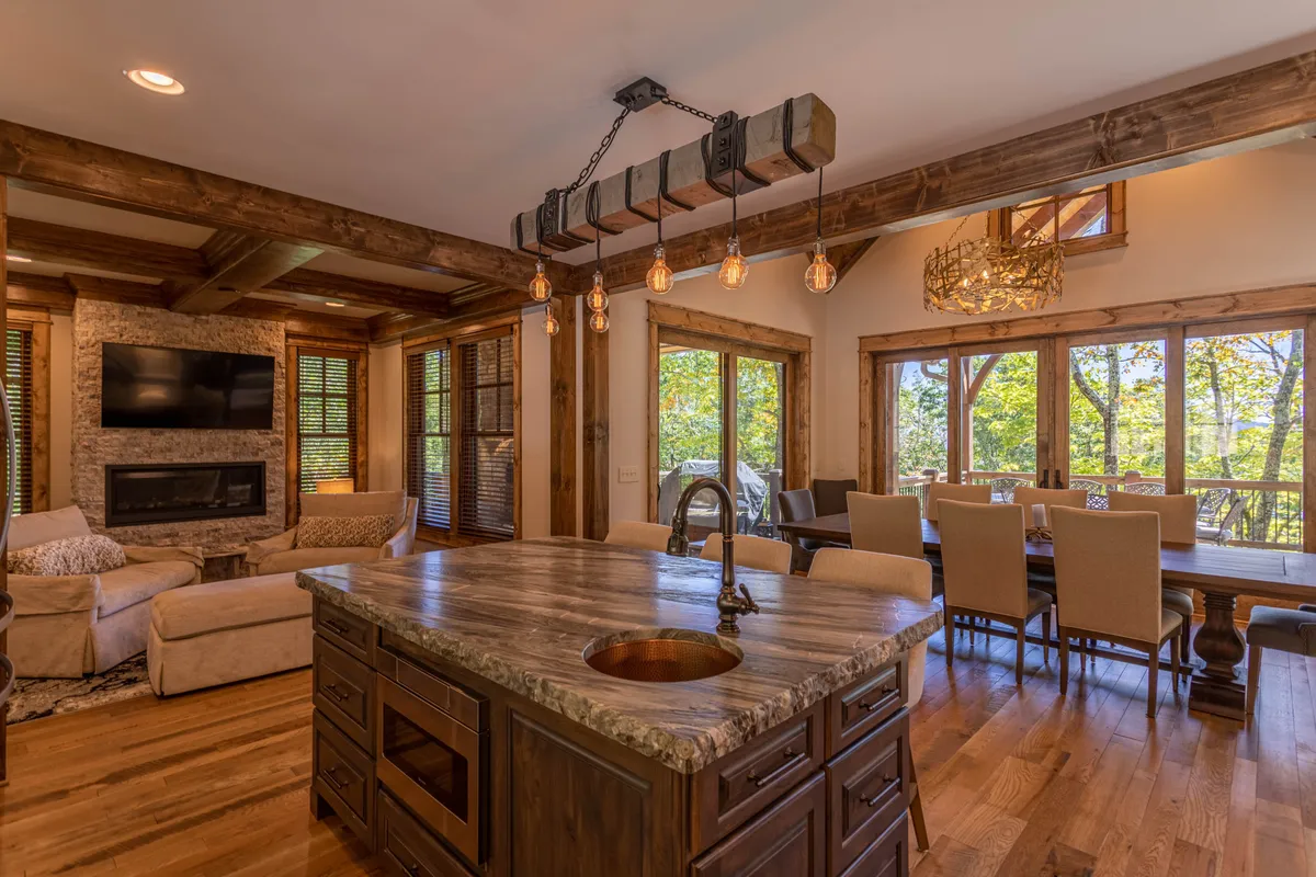 An open-concept living space with a kitchen island, adjacent dining area, fireplace, and large windows bringing in natural light. The layout allows for easy flow between the kitchen, dining, and lounging spaces—ideal for entertaining.