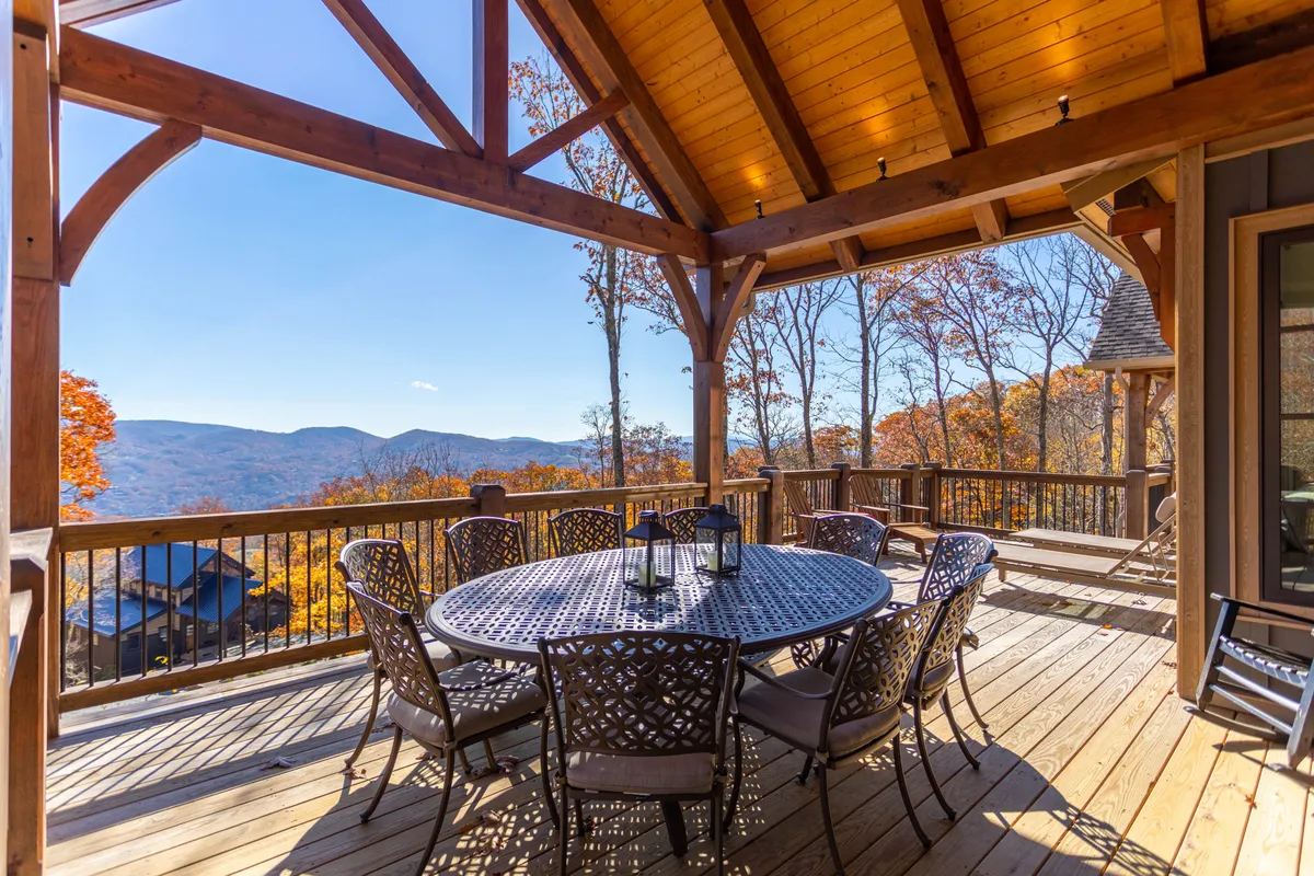 An outdoor dining table set beneath wooden beams with panoramic mountain views. The setting is relaxed and cheerful, ideal for al fresco meals and socializing in the fresh mountain air.