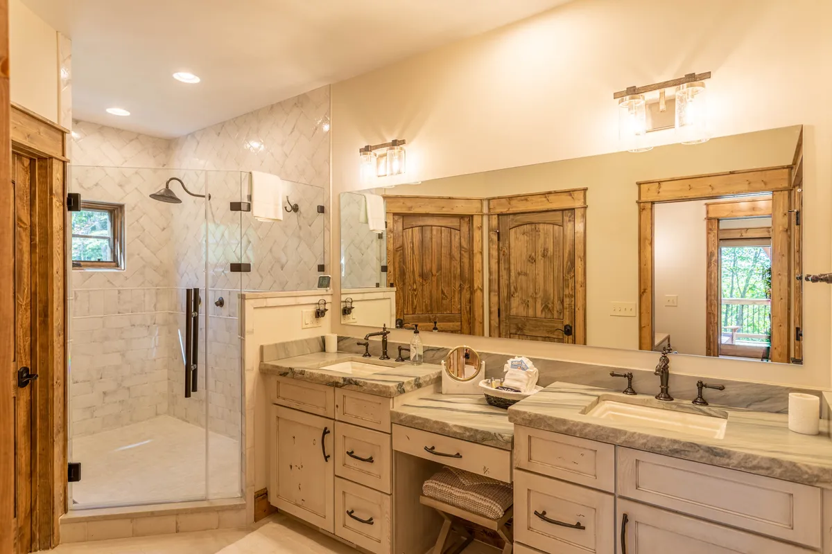 A high-end bathroom featuring a double sink vanity, walk-in shower, large mirror, and wooden doors. The tranquil feel and upscale finishes suggest a spa-like retreat, ideal for rejuvenation and privacy.