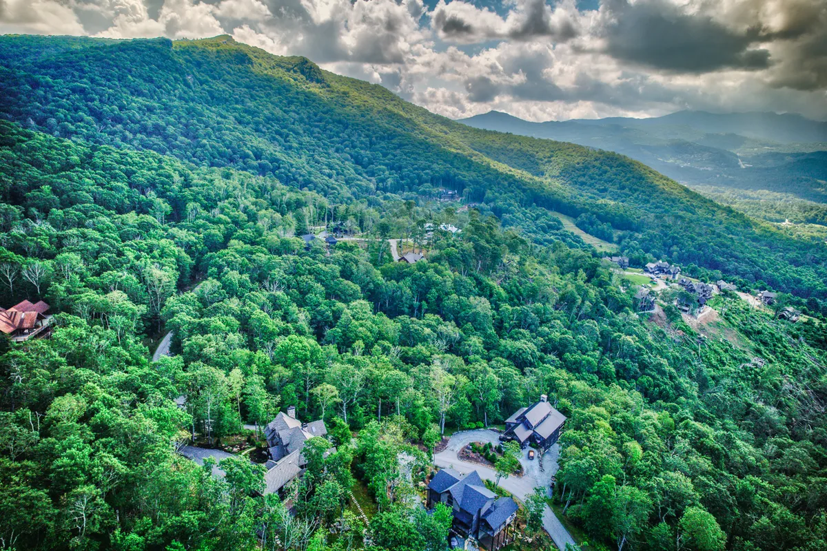 A sweeping view of a mountainous landscape with dense forests, scattered homes, and winding roads, capturing the expansive beauty and adventure potential of the High Country area.