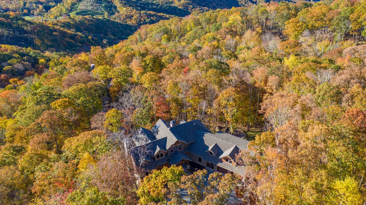 A wide view of the house nestled among trees with mountain scenery in the background. The spacious porch invites guests to relax and enjoy the stunning natural surroundings.